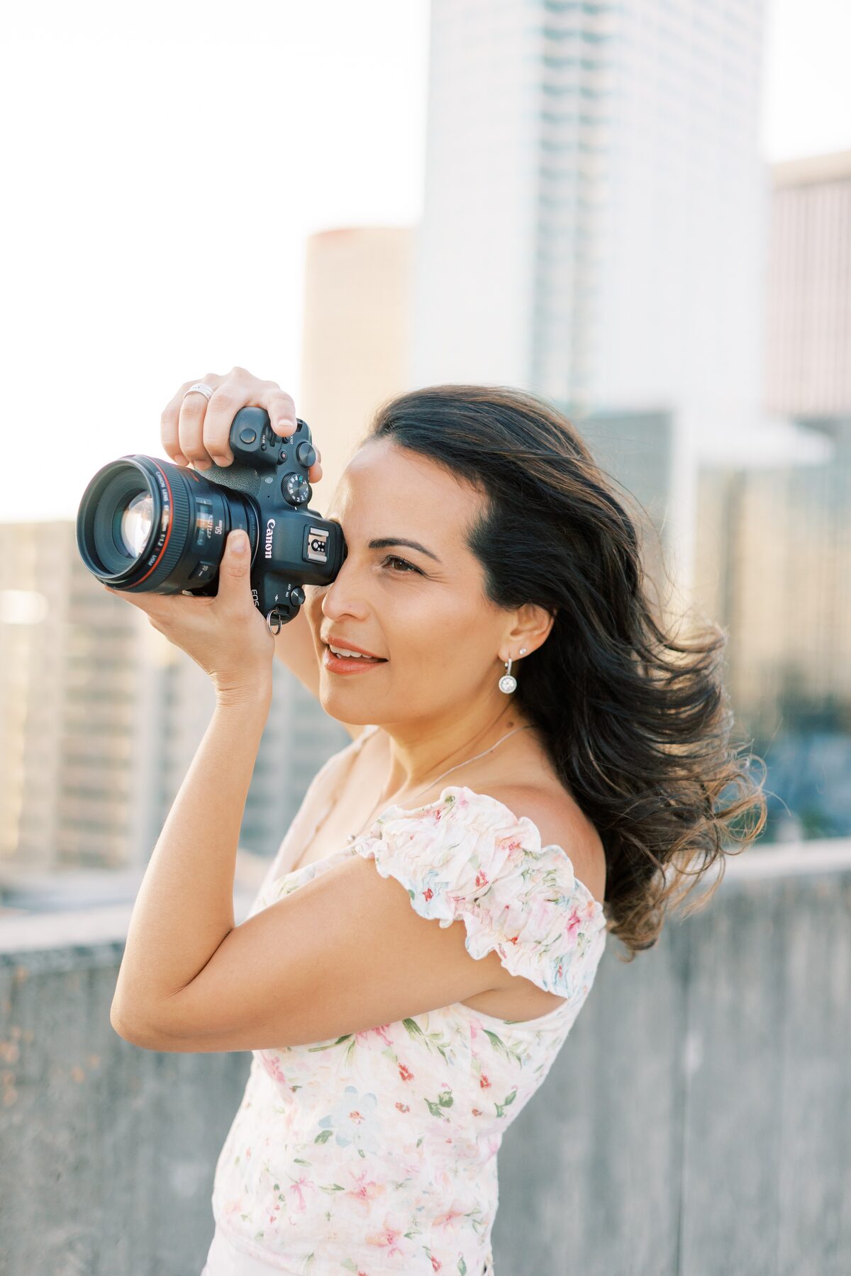 Ailyn La Torre shooting with a Canon EOS at golden hour on a Tampa rooftop, city skyline glowing behind her — Tampa Bay wedding photographer