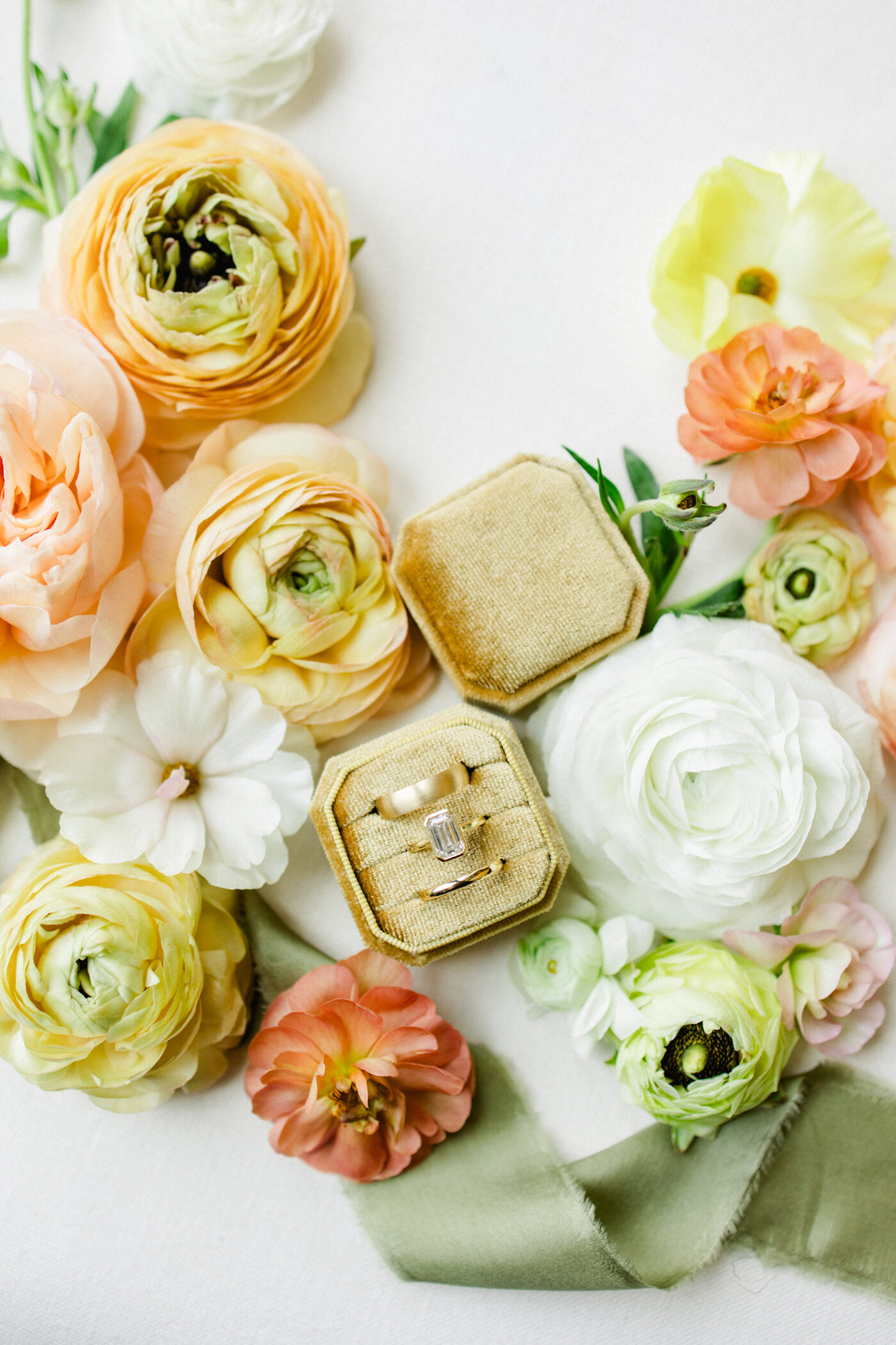 Emerald cut diamond engagement ring in an olive velvet ring box surrounded by colorful ranunculus and garden roses — Tampa Bay wedding photographer Ailyn La Torre