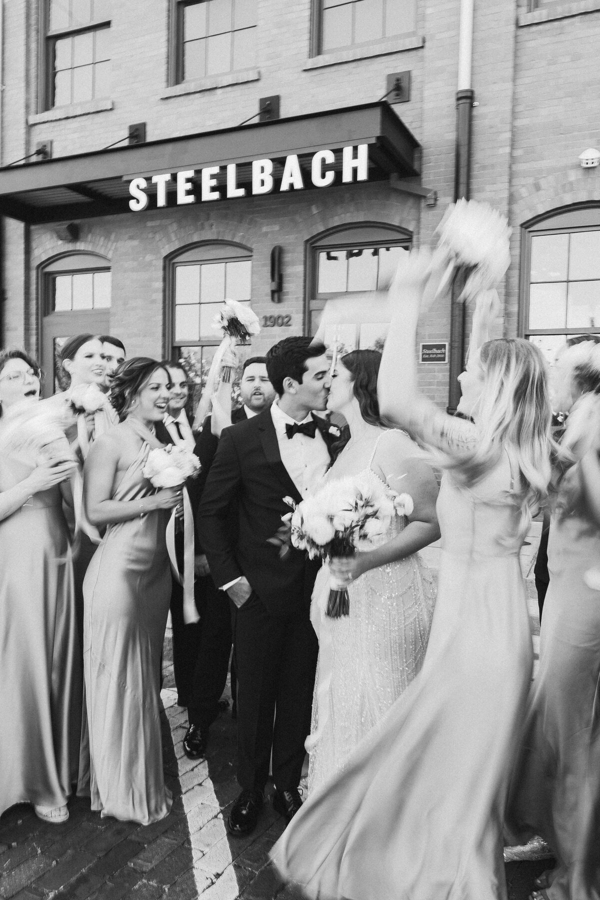 Bride and groom stealing a kiss as their wedding party celebrates outside Steelbach at Armature Works in Tampa — luxury wedding photographer Ailyn La Torre
